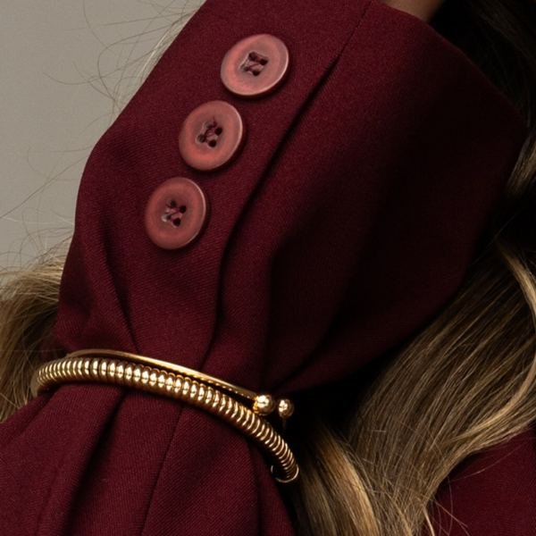 Detalhe do punho do blazer vinho com botões e pulseira dourada